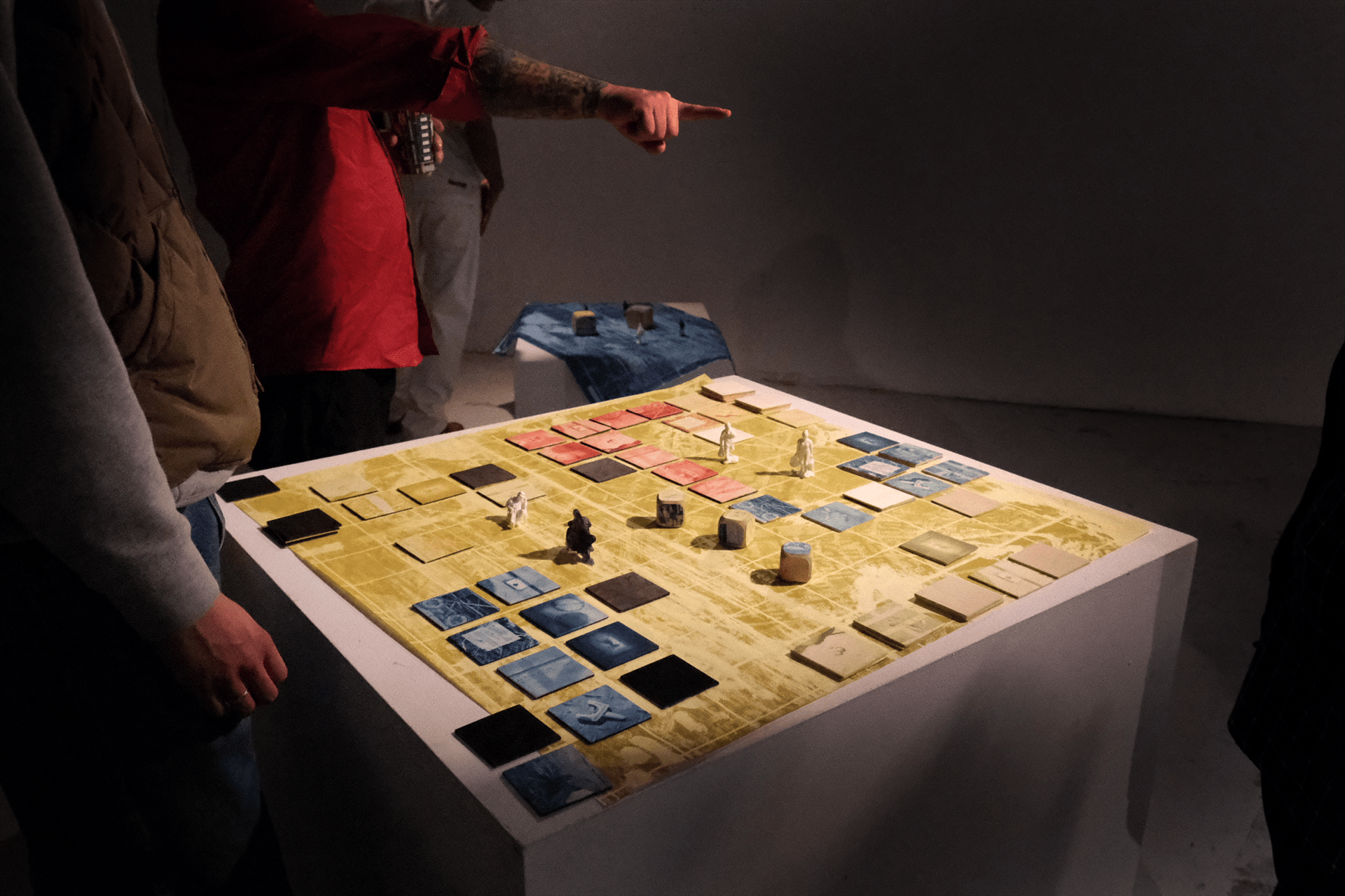 A group of people engaged in a board game on a yellow and blue game board with various colored tiles and small figurines.